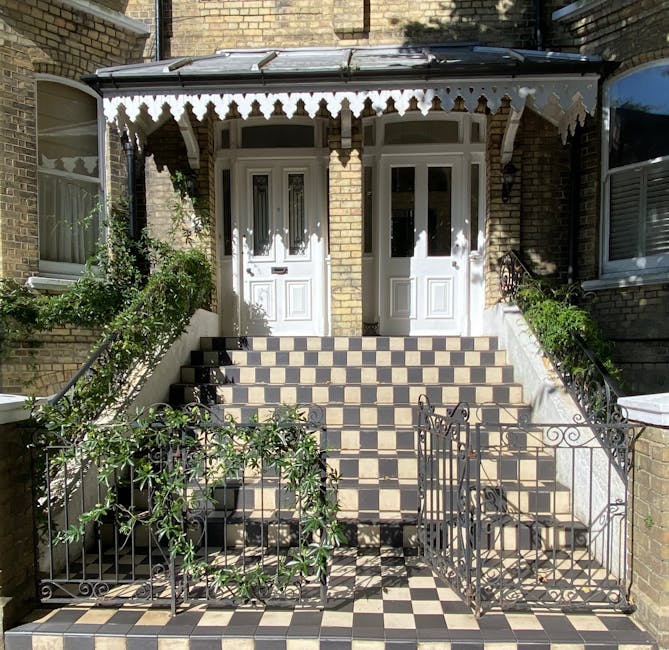 A narrow, spiral staircase inside a property with white-painted walls and a dark wooden handrail supported by decorative black metal balusters. The staircase curves around a central white column, with