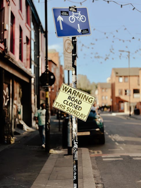A street scene in Chiswick showing a blue and white traffic sign indicating a shared bicycle and pedestrian pathway with arrows pointing in opposite directions, positioned above a yellow warning sign 